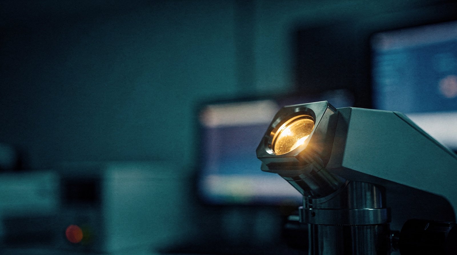 An electron-microscope column in a dark metrology bay, its viewport glowing faint warm gold