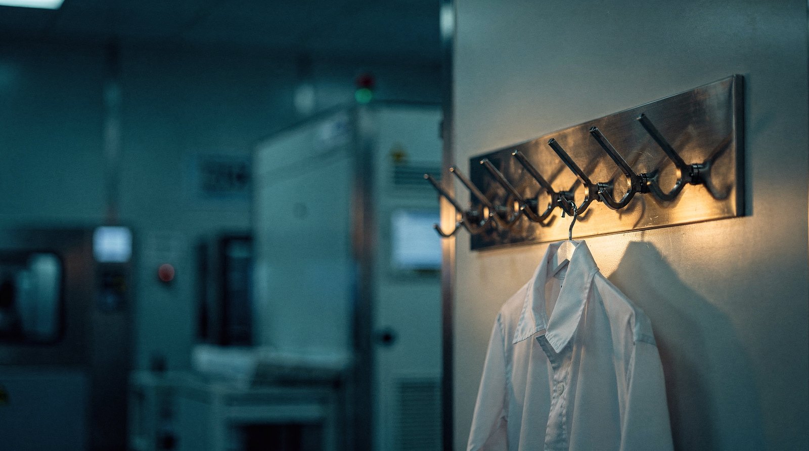 A row of empty cleanroom garment hooks, one gown hanging alone lit warm gold