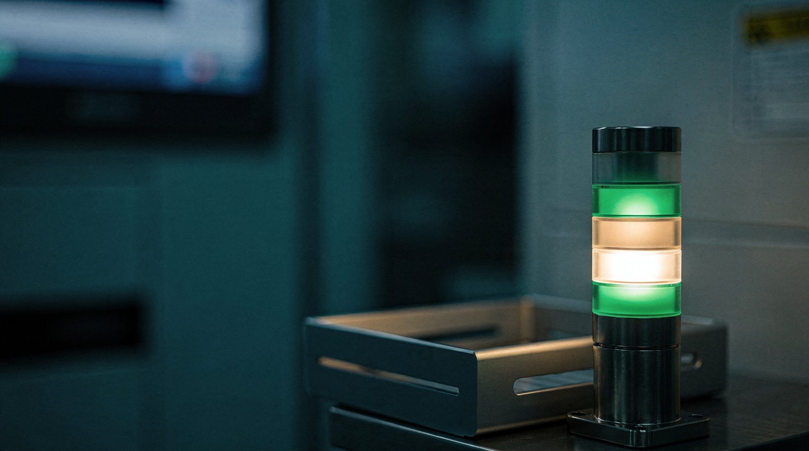 A process tool's status lamp stack with the green lamp lit, beside an empty output cassette, the empty cassette catching the warm gold light