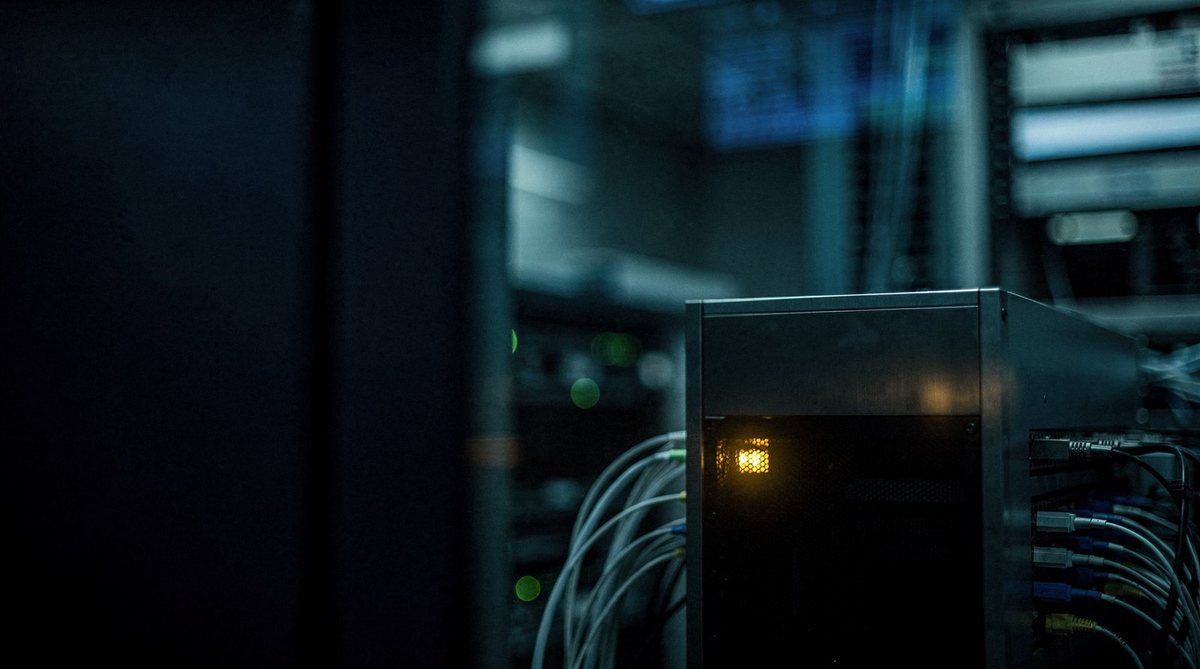 A dark server module in a fab data room with one warm gold light behind glass